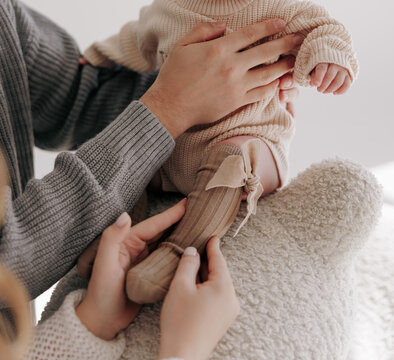Parents holding newborn baby wearing beige knitted clothing and cute socks.