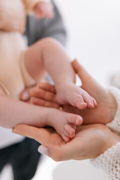 Mother hands gently hold tiny feet of newborn baby in light cozy room.