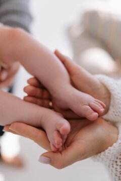 Mother hands gently hold tiny feet of newborn baby in light cozy room.