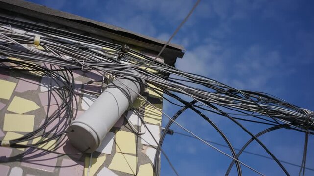 Fiber optic cables connect to a splice enclosure on a rooftop wall under a blue sky. This exterior hardware junction secures wired data lines for high-speed internet distribution.