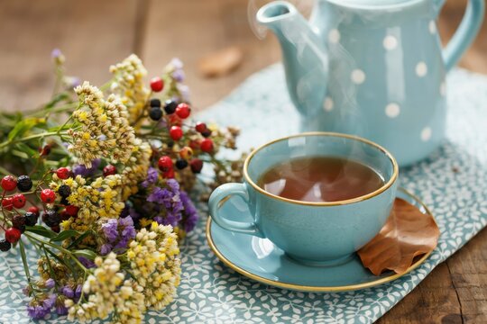 Steaming cup of herbal tea with a teapot and a bouquet of dried wildflowers