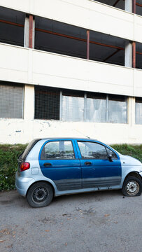 Older Daewoo Matiz parked beside an industrial building, showing the condition of an inexpensive used compact car and the effects of long term vehicle ownership