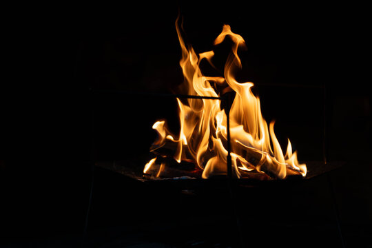 Tall wavy campfire flames burning in a fire pit against a dark night background