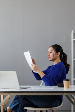 Young asian woman analyzing financial data, reading business report, reviewing documents, planning strategy, managing finances, ensuring productivity, working in modern office environment