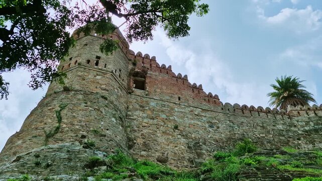 A rounded stone bastion and crenellated wall rise beneath trees at Kumbhalgarh Fort on an Udaipur trip.