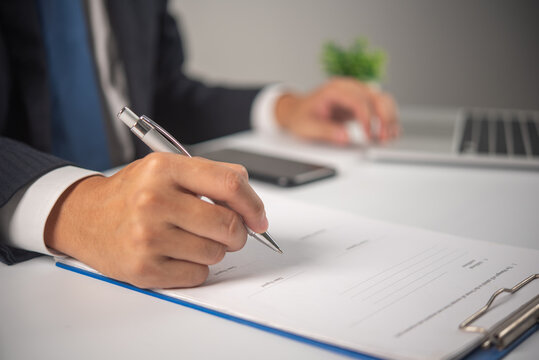 Business professional signing official document at desk with laptop