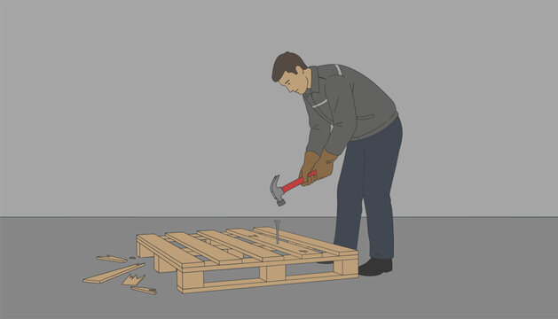 Warehouse worker uses a hammer to repair a wooden pallet on the floor of an industrial workshop.