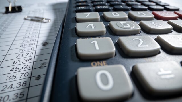 Focusing calculator keypad showing worn gray keys on desk with ledger, binder and paperclip