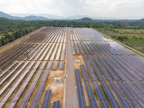 Drone shot of solar power plant array on ground generating renewable energy in rural area with mountain scenery. Clean energy, ESG, and sustainable technology concept. Human-created,