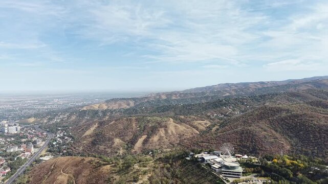 Cinematic 4K drone video panning across Kok Tobe hill in Almaty, Kazakhstan at sunny September morning, revealing majestic Tian Shan mountains, morning smog over city skyline