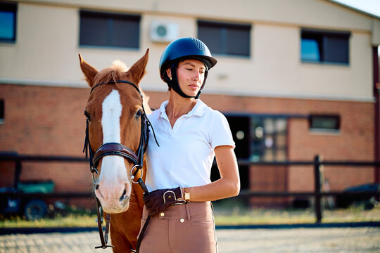 Woman rider wearing a helmet and riding gear standing with her chestnut horse, fostering a strong bond at an equestrian stable