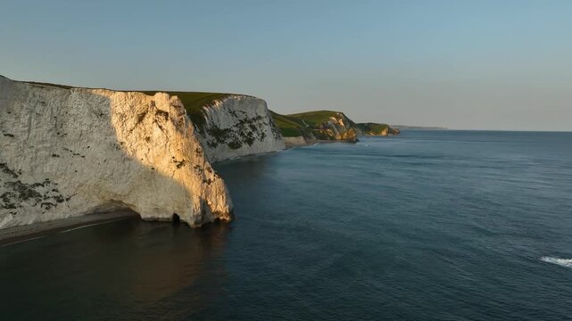Sideways aerial tracking shot of white chalk cliffs at golden hour