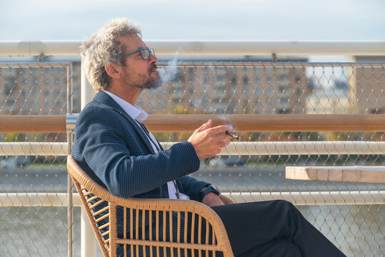 Senior man in eyeglasses smoking cigarette outdoors in city