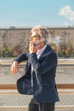 Senior man in eyeglasses smoking cigarette outdoors in city
