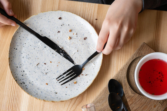 People eating dessert at a table with empty plates, utensils, and a small bowl of red sauce