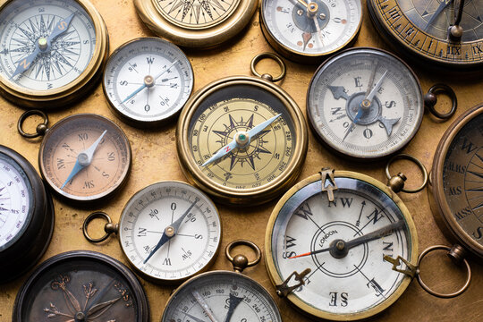 Collection of antique compasses arranged on a worn brass surface, featuring vintage navigation instruments, aged metal, and historical details. A nostalgic still life evoking geography, maritime.