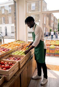 Black grocer arrange fresh fruit in neighborhood shop