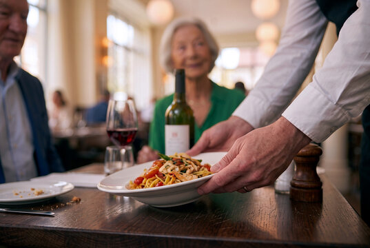 Waiter serve pasta to older couple at restaurant