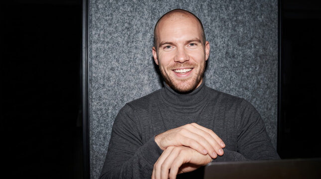 Smiling bald man working on laptop in dark office