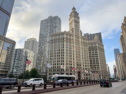 CHICAGO, IL, JUN 17, 2026: The Wrigley Building&rsquo;s white clock tower beside the Michigan Avenue Bridge, with flags, a CTA bus and a taxi in the foreground