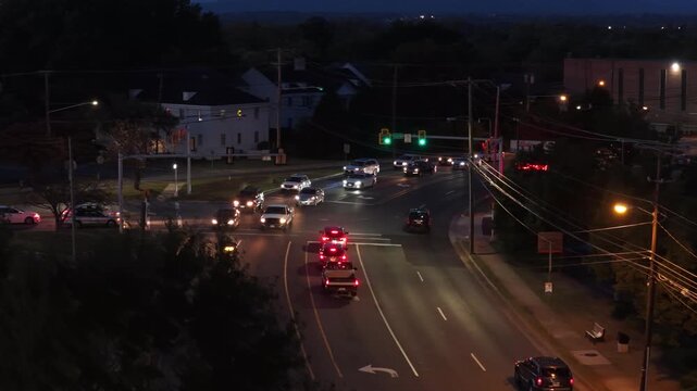 Telephoto of a busy signalized intersection on Fort Avenue in Lynchburg, Virginia at night, a queue of red taillights, green signals, sodium streetlights, power lines and a white house. Aerial view