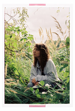 A woman looks up through layered foliage and meadow grass