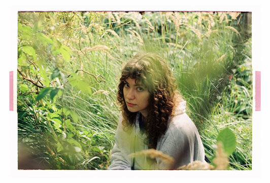 A woman looks up through layered foliage and meadow grass
