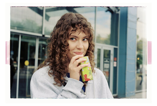 A young woman sips a juice box outside a city shopfront