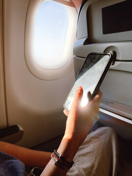 Person Using Smartphone on Airplane Seat by Window