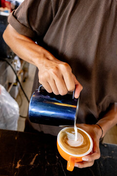 Anonymous barista pouring milk to create latte art in coffee cup