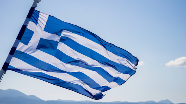 Greek flag waving on a pole, sunny blue sky, Greece