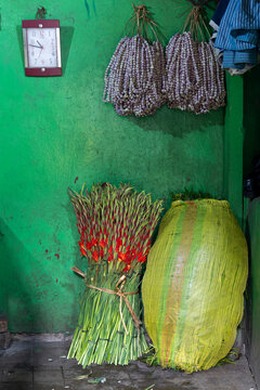 Bunch of red gladiolus beside a large woven bundle against a green wall with hanging garlands at the flower market, West Bengal, Kolkata, India