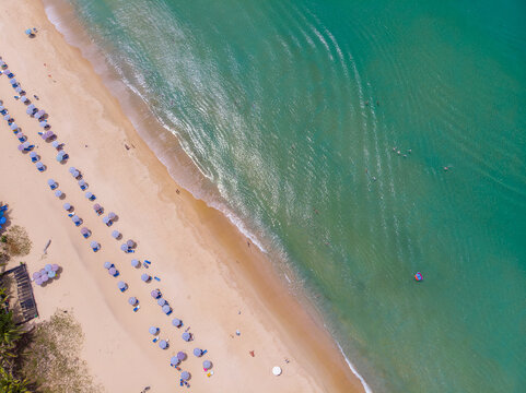 Aerial top view of sandy beach with beach umbrellas, sunbeds, and clear emerald ocean water