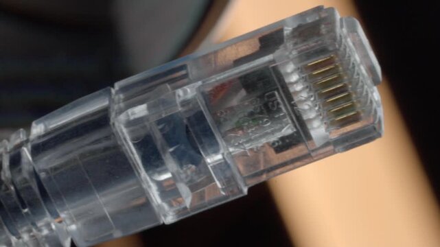 Transparent Ethernet connector showing gold contacts and internal wiring detail. Closeup view highlights clear plastic housing and network cable connection technology.