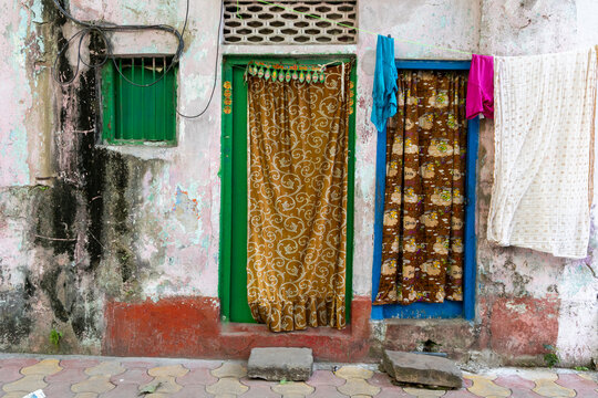 Weathered wall with a green door and window curtains patterned with swirls and hanging laundry, West Bengal, Kolkata, India