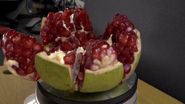 Spinning cut pomegranate arranged on a rotating platform with juicy red seeds and pale inner flesh exposed against a dark background during close up food presentation