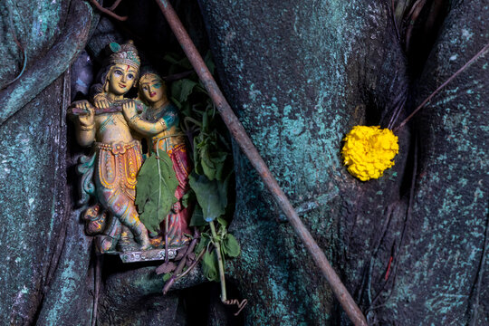 Painted clay figurines of a divine couple tucked in a tree trunk with a marigold flower, West Bengal, Kolkata, India