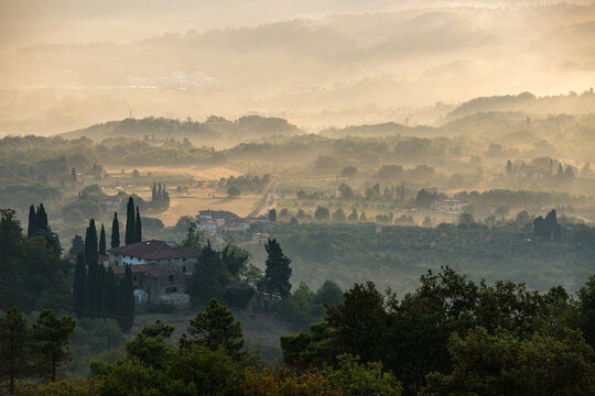 Scenic morning view over foggy Tuscan hills and rural farmhouses surrounded by cypress trees at sunrise, Italy
