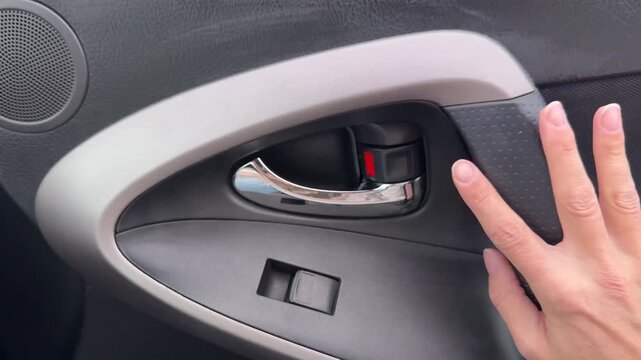 Horizontal close up view of a female hand pulling an interior handle to open a car door from the inside cabin