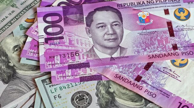 Philippine peso (PHP) banknotes are falling on top of 100 US dollar (USD) bills. Concept of exchange rate, global finance, and international economy.  Real time footage