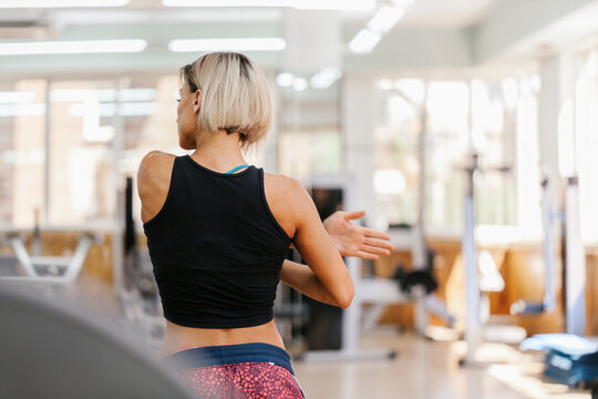 Woman stretching shoulder in bright gym training room