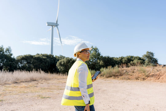Female engineer inspecting wind turbine field with smartphone