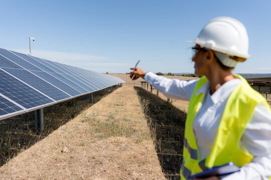 Female engineer inspect solar panel array at renewable energy farm