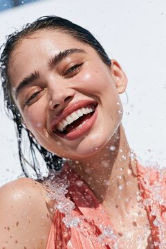 Laughing woman closeup with water splash in coral outfit for summer banner and skincare background use