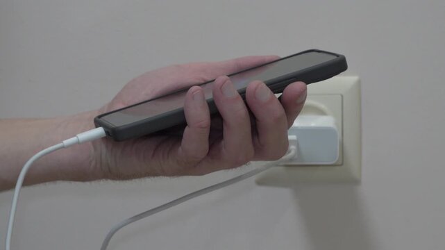 Man hands plugging a white charging cable into a smartphone close up, Connecting a mobile phone to a charger near a wall socket