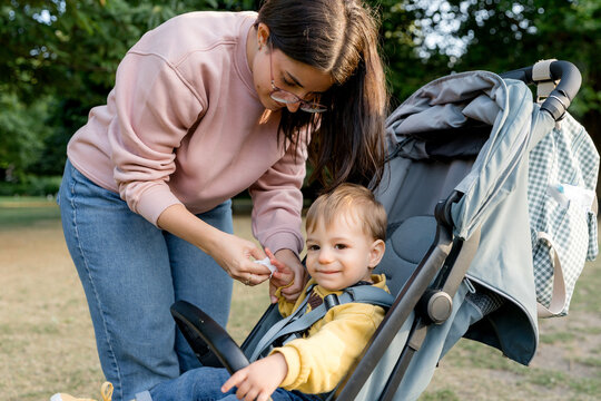 Mother secure toddler in stroller at city park