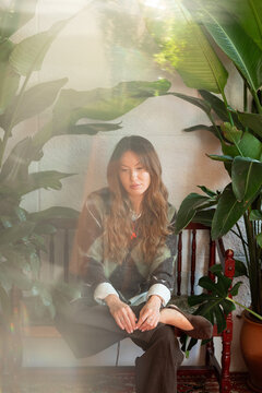 Woman sitting among potted plants in sunlit interior