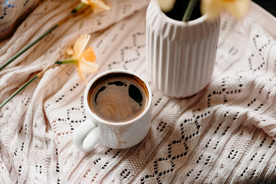 Coffee and daffodil still life on a cozy knitted blanket