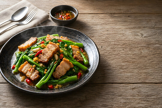 Stir-fried Chinese kale with crispy pork belly Kana Moo Krob served hot on a ceramic plate
