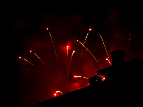 Red fireworks illuminate night sky above rooftop silhouette